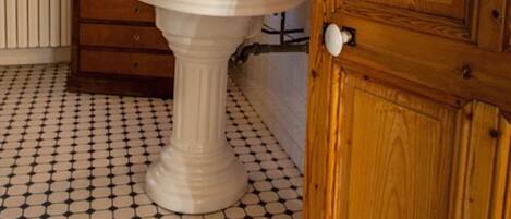A bathroom with a white pedestal sink, wooden cabinets, a tiled floor, and a wooden door.