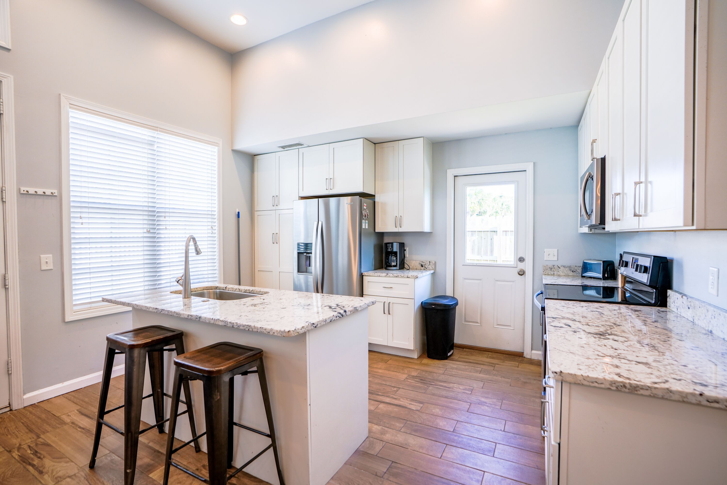 A modern kitchen with white cabinets, a stainless steel refrigerator, and a granite countertop.