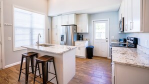 Una cocina moderna con armarios blancos, un refrigerador de acero inoxidable y una encimera de granito.