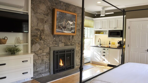 A bedroom with a stone fireplace, a television, and a bed.