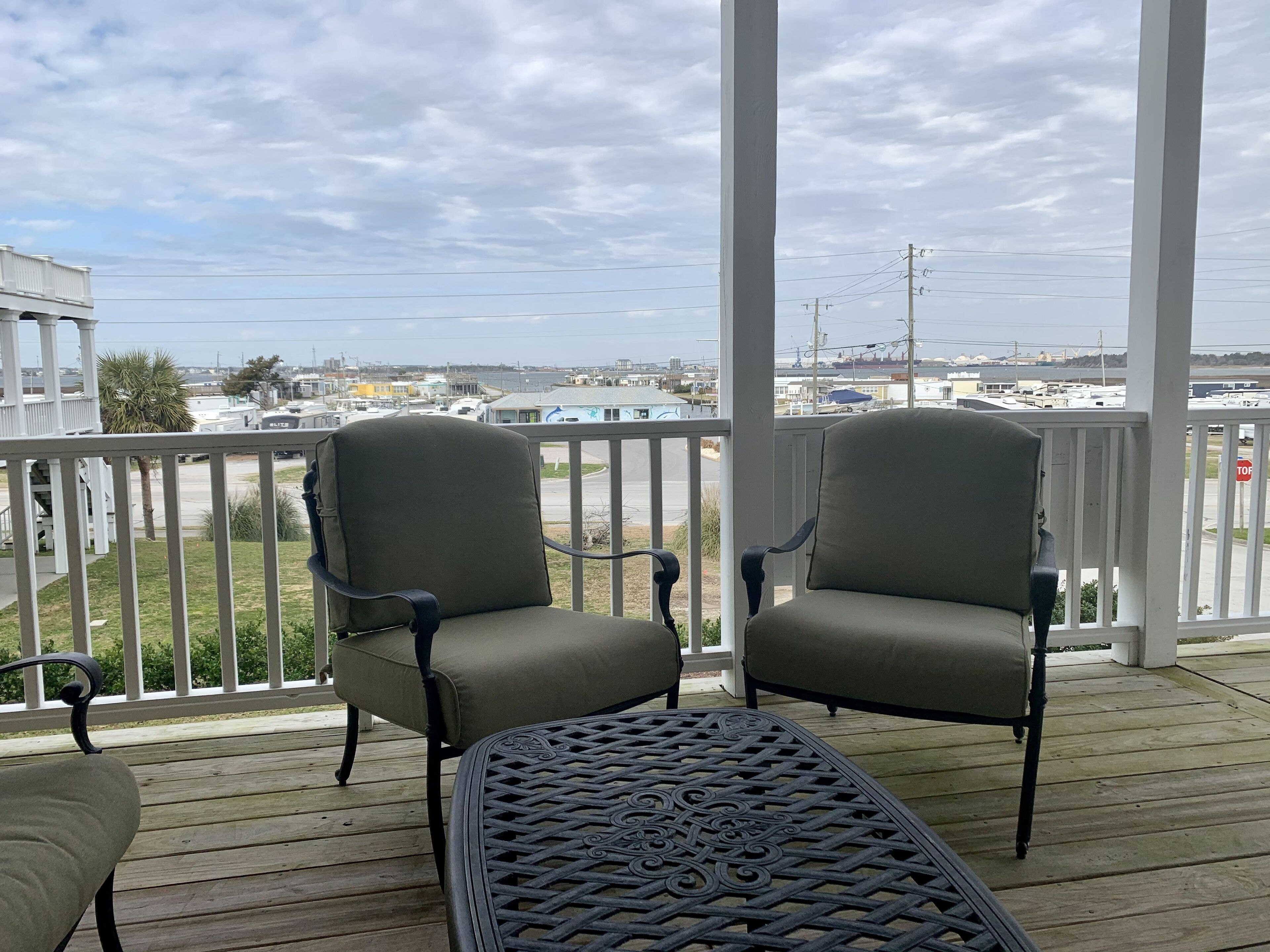 A covered outdoor area with two chairs and a table, overlooking a marina with boats and buildings.