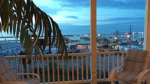A wooden deck with two wicker chairs, overlooking a marina with boats and buildings. - Beautiful Retreat with Ocean & Sound Views (Atlantic Beach)