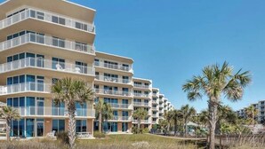 A multi-story hotel with balconies, palm trees, and a beach view.