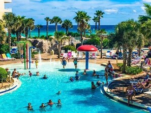 Un espace piscine agrémenté de plusieurs éléments aquatiques, de palmiers et de chaises longues.
