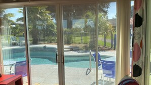 A room with a sliding glass door leading to a backyard with a swimming pool, outdoor furniture, and a view of palm trees.