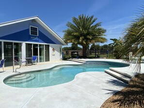 A swimming pool with a curved design, a blue building with large windows, and a palm tree. -  SWIM , SWIM , SWIM - Cottage w/ Private Pool on Horse Farm, Close to Ocala  WEC (Ocala)