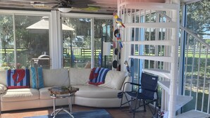 A sunroom with a white curved sofa, a blue and red patterned throw, a small table, and a blue folding chair.