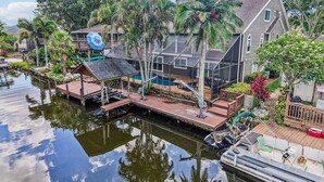 A house with a dock extending into a body of water, surrounded by palm trees and a small deck area.