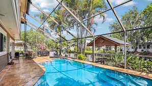 A swimming pool with a glass enclosure, surrounded by palm trees and a view of a house.
