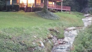 Eine Lodge mit rotem Dach und Balkon, umgeben von Grünpflanzen und einem kleinen Bach.