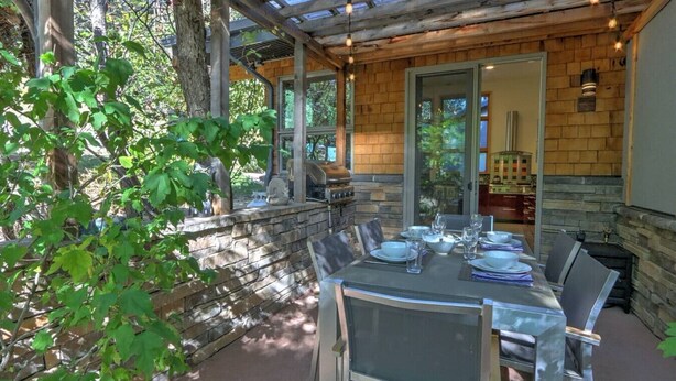 Un espacio al aire libre para comer con un muro de piedra, una parrilla y una mesa preparada para cuatro personas.