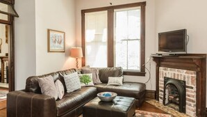 Un salon avec un canapé en cuir marron, un petit pouf, une cheminée et un téléviseur posé sur un meuble.