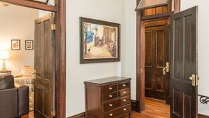 Un couloir avec des portes en bois, une commode en bois sombre et un tableau encadré accroché au mur.