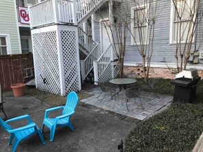 Une terrasse avec deux chaises bleues, une petite table ronde et un barbecue.