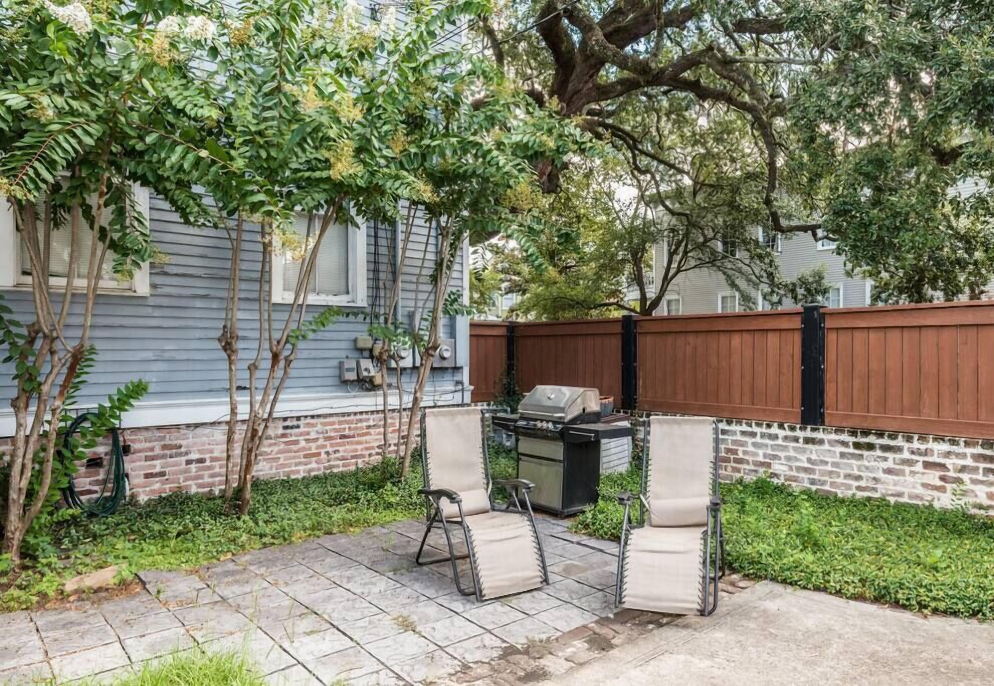 Un jardin avec une terrasse, deux chaises, un barbecue et une clôture en bois.