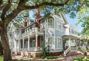 Une maison à deux étages avec un porche, une cheminée en briques et un grand arbre devant.