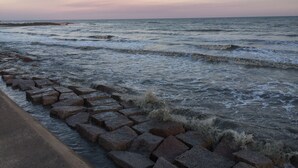 Paesaggio costiero con onde che si infrangono su un molo roccioso.