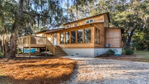 A wooden cabin with a deck, surrounded by trees and a gravel driveway. - Riverfront House With Dock Sleeps 8 (St Simons Island)