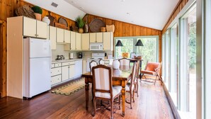 A modern kitchen with wooden cabinets, a dining table with chairs, and large windows. - Riverfront House With Dock Sleeps 8 (St Simons Island)