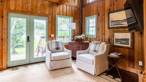 A wooden interior with two white armchairs, a wooden desk, and a small table. - Riverfront House With Dock Sleeps 8 (St Simons Island)