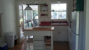 Una cocina compacta con una mesa de madera, armarios blancos, una encimera roja y un ventanal que proporciona luz natural.