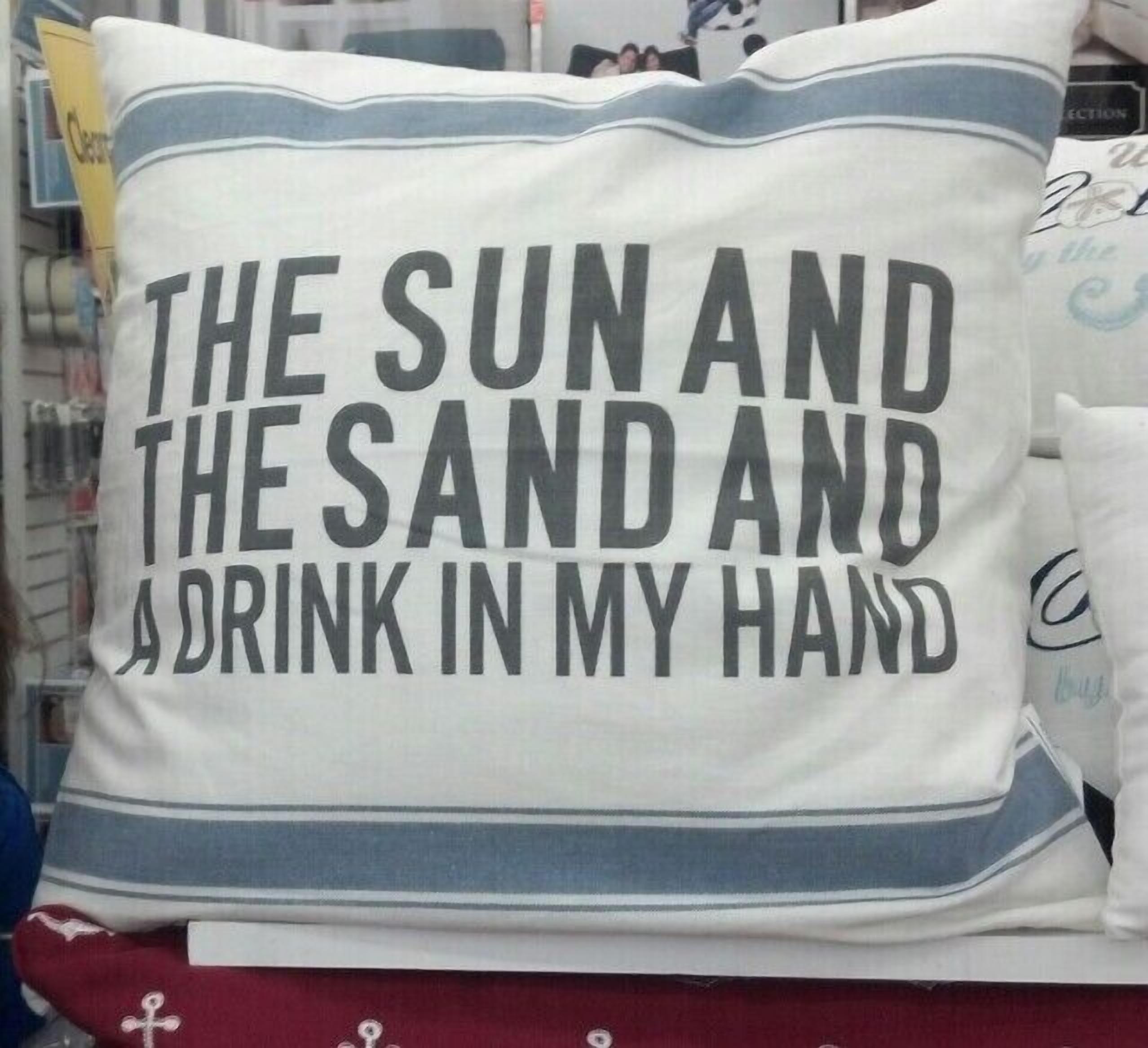 A pillow with the text "THE SUN AND THE SAND AND A DRINK IN MY HAND".