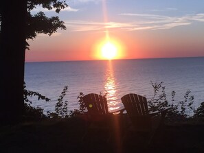 A sunset over the ocean with two Adirondack chairs facing the water.