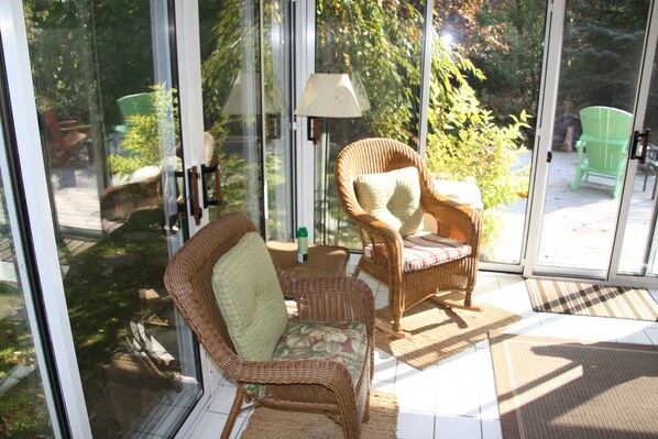 A sunlit room with wicker furniture, including two chairs and a table, and a glass door leading to an outdoor area.