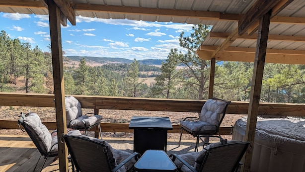 An outdoor deck with a table and chairs, a hot tub, and a scenic view of trees and hills. - Sandpiper 40ft RV @EvansCliff /HotTub on Covered Deck! new 2026 location (Hot Springs)