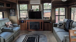 A cozy RV interior with a fireplace, a TV, and a sofa. - Sandpiper 40ft RV @EvansCliff /HotTub on Covered Deck! new 2026 location (Hot Springs)