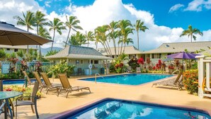 Un área de piscina con sillones de descanso, sombrillas y palmeras.
