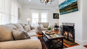 A cozy living room with a fireplace, a large window, and a chandelier.
