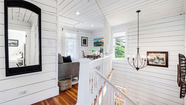 A spacious room with wooden floors, a white staircase, and a dining area with a table and chairs.