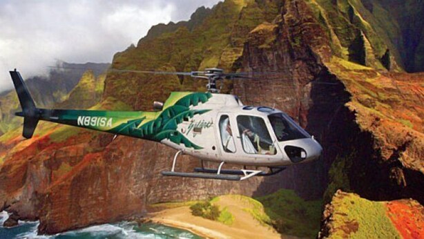 A helicopter with a green and white design flying over a coastal landscape with cliffs and ocean. - Best Deal in Town gorgeous Kauai beach resort, romantic, fun and yoga "zen" (Lihue)