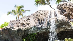A pool with a waterfall feature, surrounded by rocks and greenery.