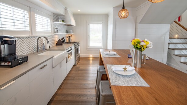 Een moderne keuken met witte kasten, een houten aanrecht en een zithoek met een houten tafel en bank.