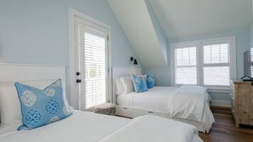 A bedroom with two beds, a wooden dresser, and a window with blinds.