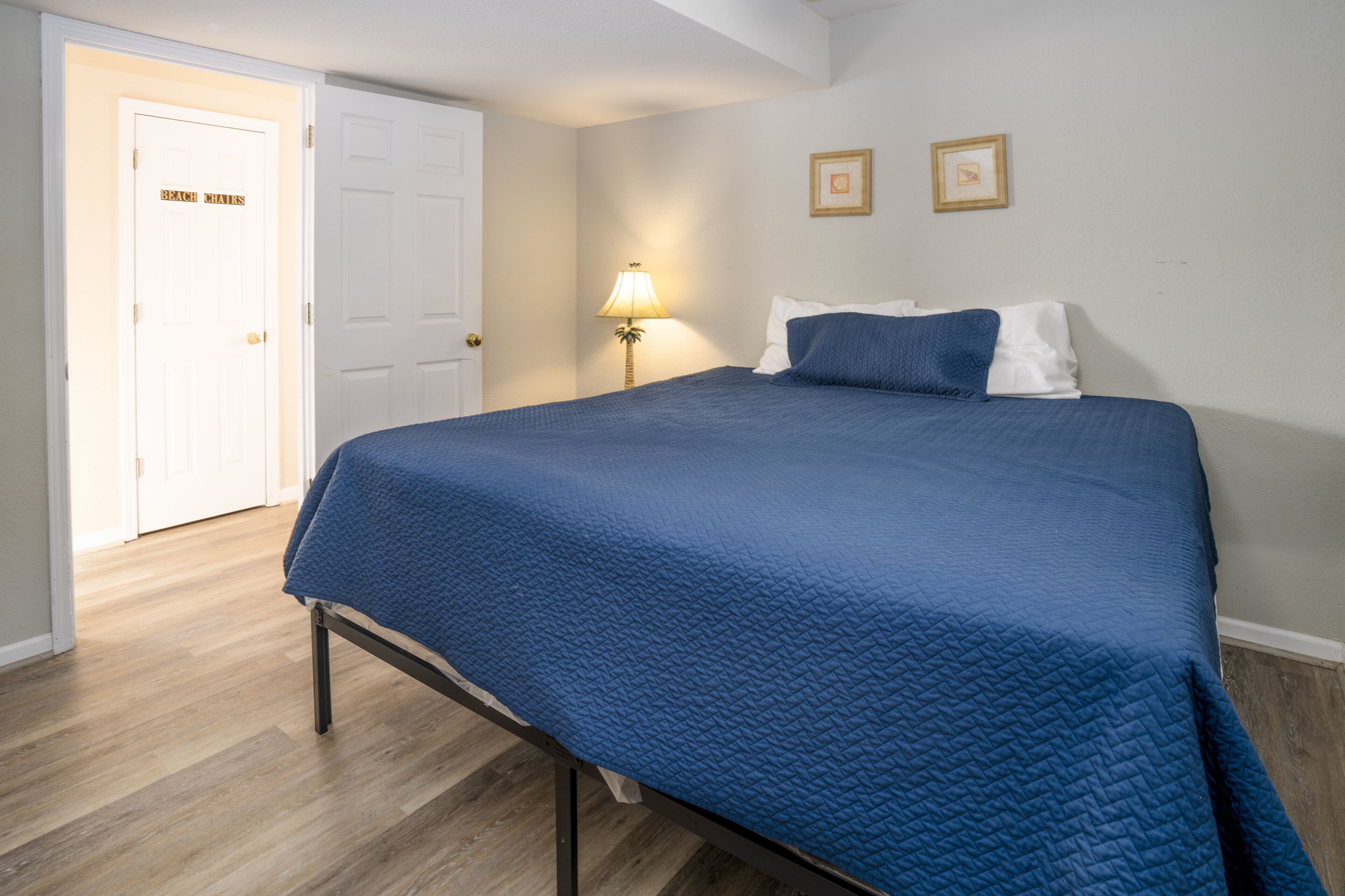 A bedroom with a bed, a door, a lamp, and two framed pictures on the wall.