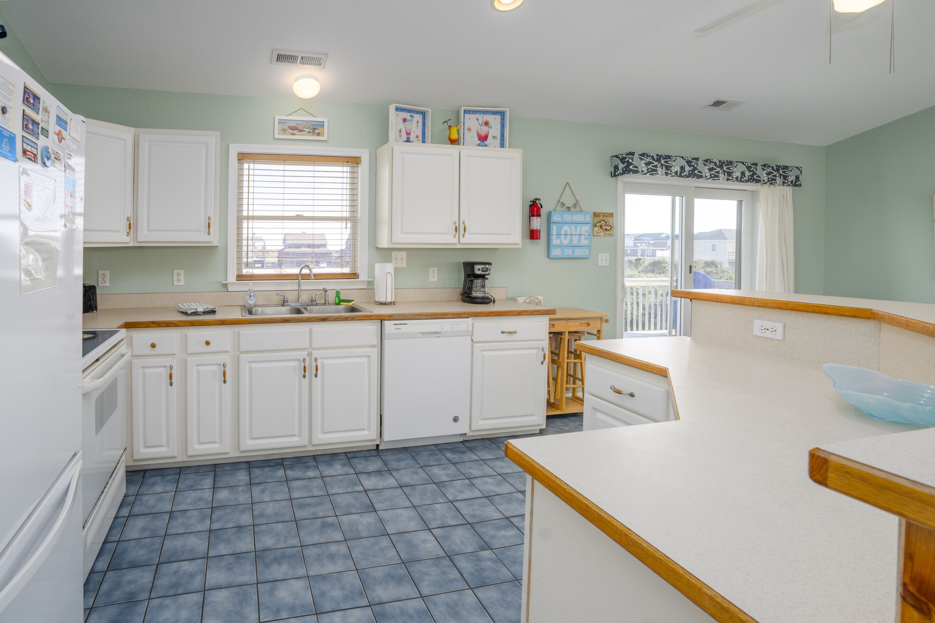 A kitchen with white cabinets, a dishwasher, a coffee maker, and a window with blinds.