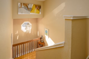 A staircase with wooden railings, a hanging light fixture, and artwork on the walls.