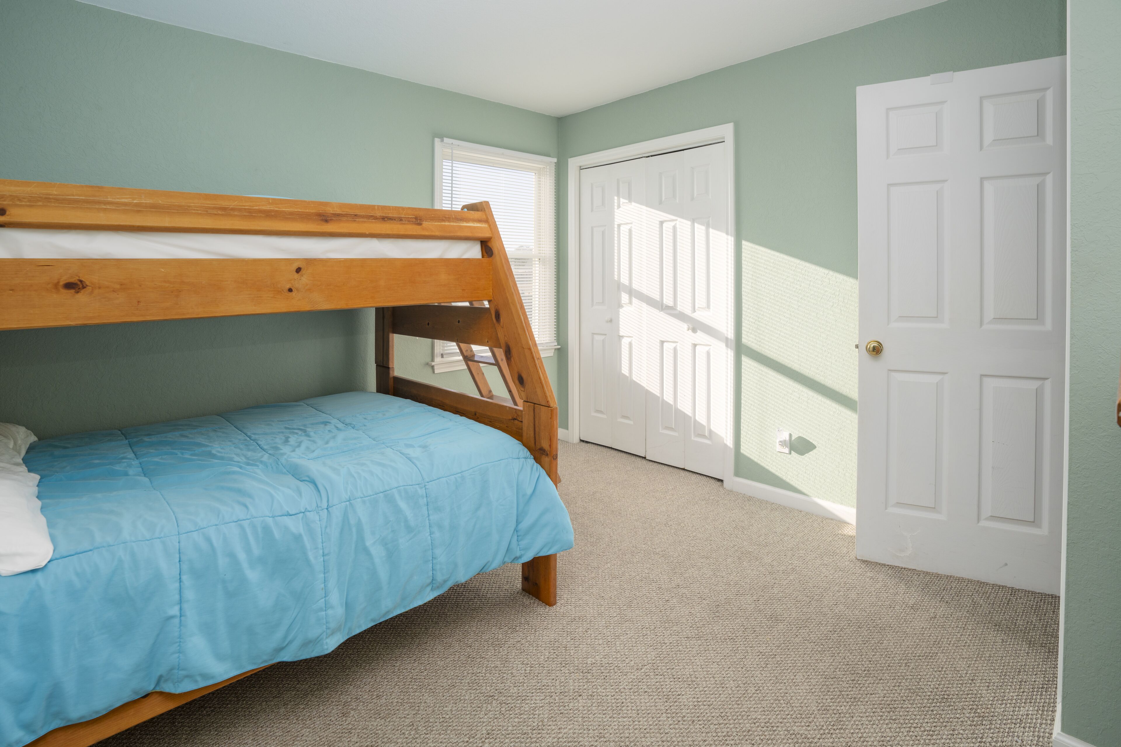 A bedroom with a bunk bed, a door, and a window.