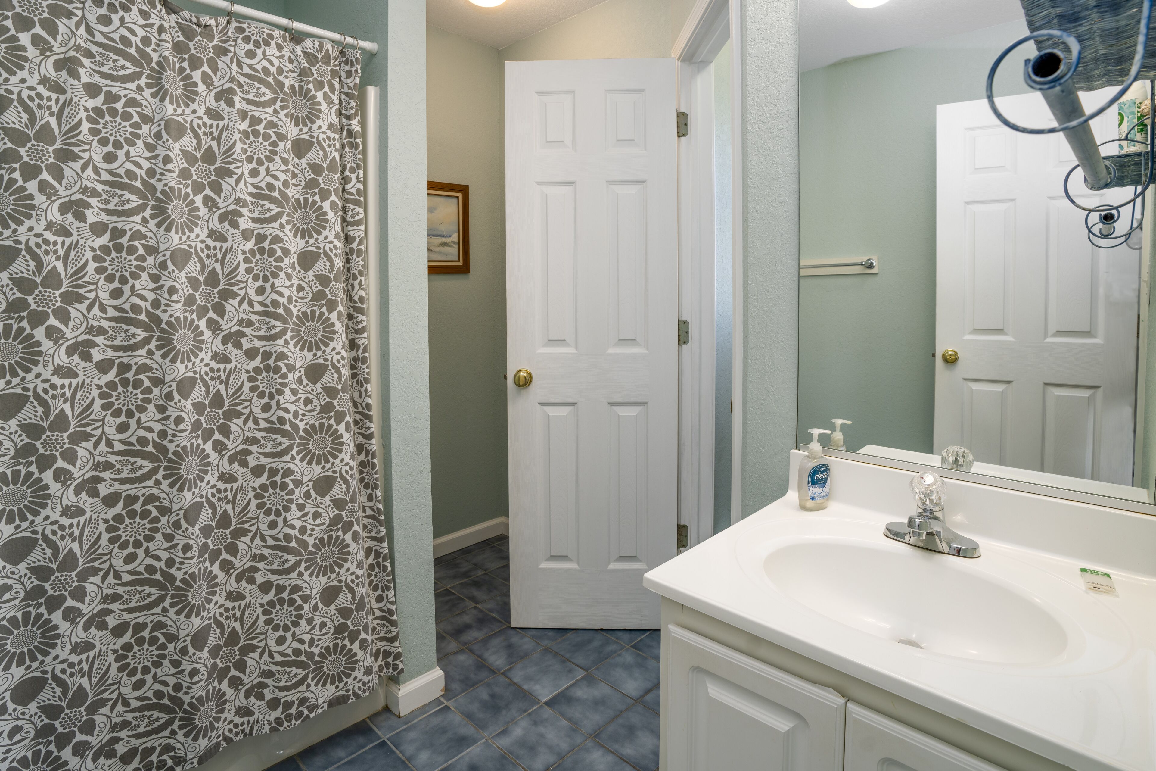 Une salle de bain avec un lavabo blanc, un miroir et un rideau de douche à motifs floraux.