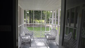A covered porch with white wicker chairs and a white fence.