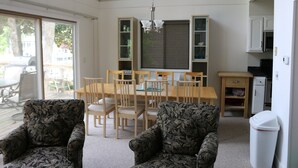 A living room with two patterned armchairs, a dining table with chairs, a chandelier, and a kitchen area with cabinets and appliances.