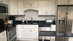 A modern kitchen with white cabinets, stainless steel appliances, a black countertop, and a built-in water dispenser.