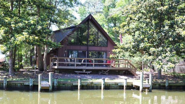 A cabin with a deck overlooking a body of water, surrounded by trees.