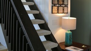 A staircase with a black handrail and carpeted steps, a wall-mounted picture frame, and a table with a lamp and a book.