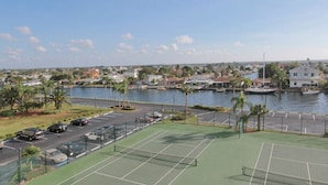 En tenniskort som ligger intill en parkeringsplats, med utsikt över en småbåtshamn och bostadshus på andra sidan av vattnet.