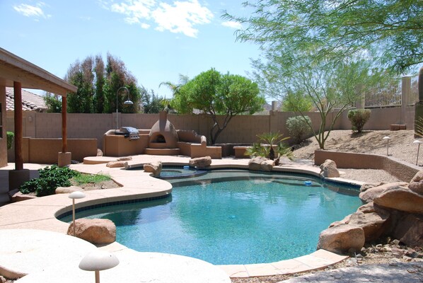 A swimming pool with a curved design, surrounded by rocks and a pergola. -  Executive Relaxed Living Home 5BR/3B Pool & Spa in Estrella Mt Ranch (Goodyear)