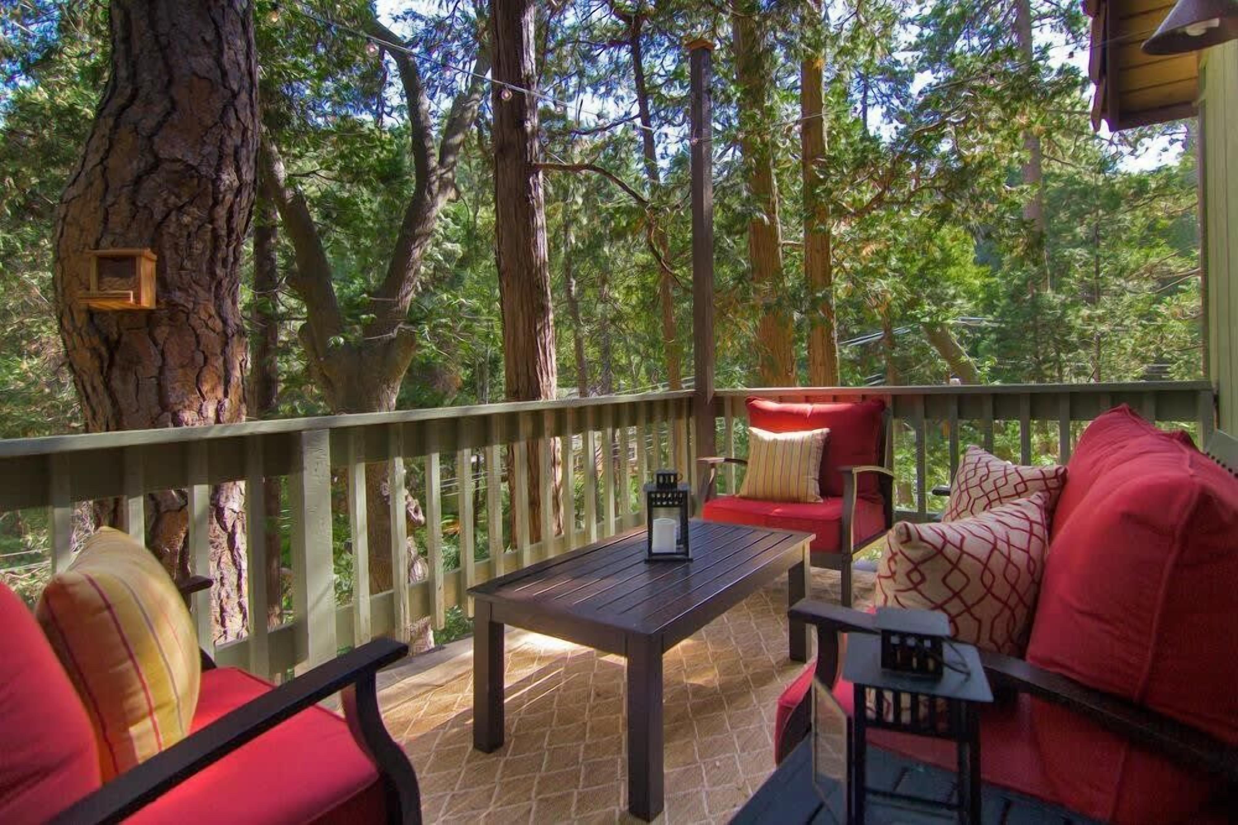 An outdoor deck with a wooden table and red furniture, surrounded by trees.
